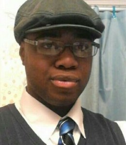 Photo of Christopher Holliman, a young man with brown skin and dark brown eyes. He is wearing glasses, a newsboy cap, and a formal shirt, vest, and tie.