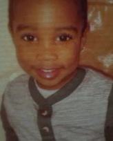 Photo of Tevaun Williamson, a little boy with dark-brown eyes and brown skin, wearing a gray sweater and smiling for the camera.